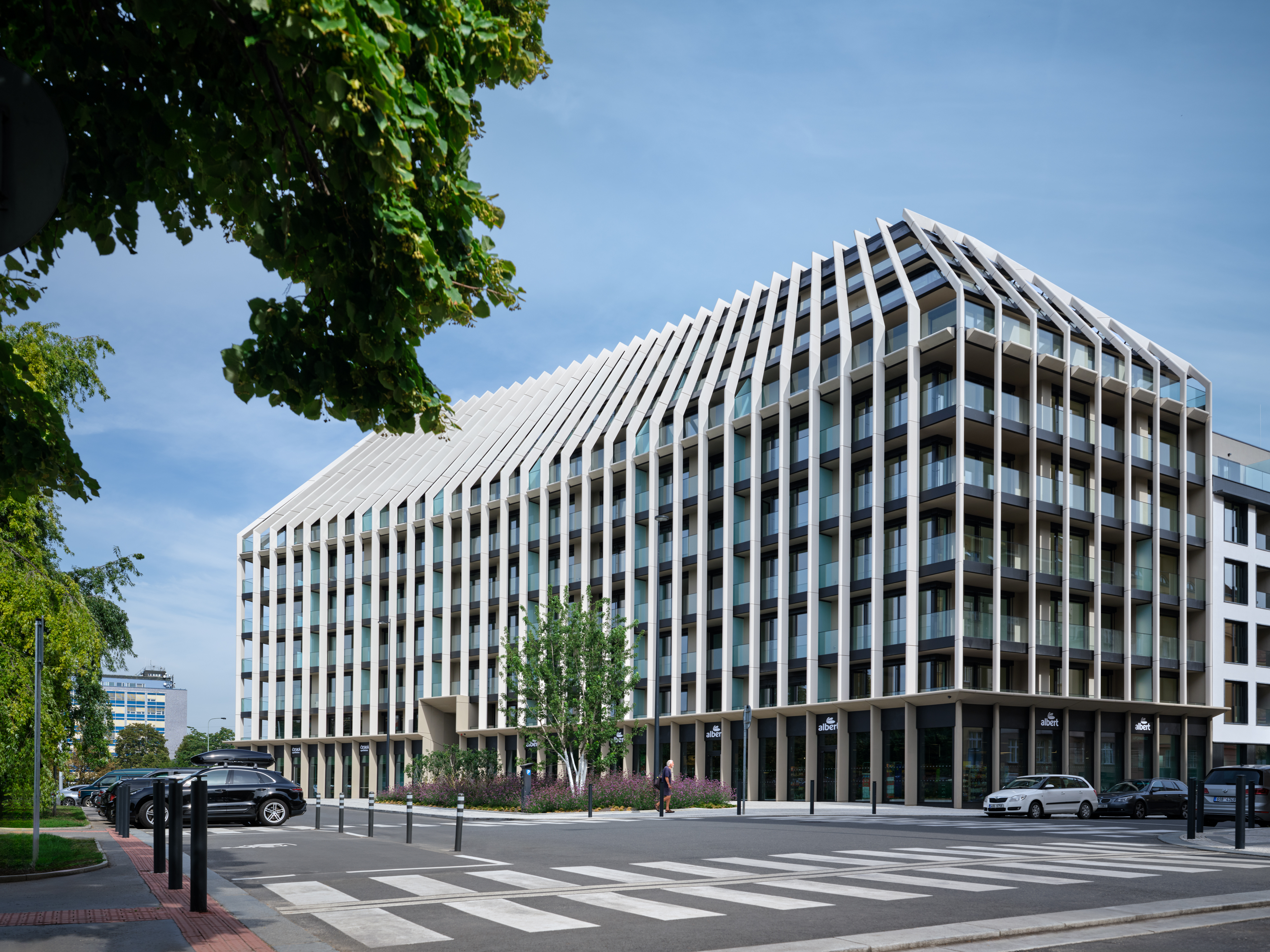 Moderní budova Victoria Palace s výraznou fasádou tvořenou svislými bílými lamelami a prosklenými balkony, obklopená zelení.