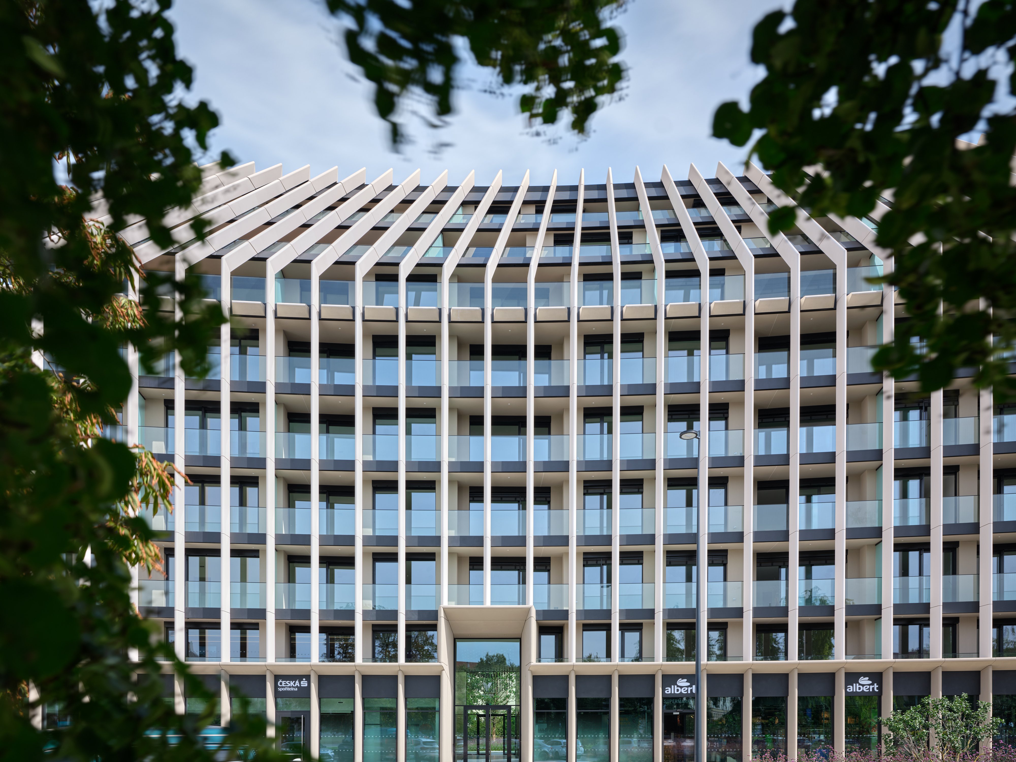 Moderní budova Victoria Palace s výraznou fasádou tvořenou svislými bílými lamelami a prosklenými balkony, obklopená zelení.